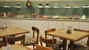A buffet area with various food items and a seating area with wooden tables and chairs. - Rede Andrade Navegantes (Recife)