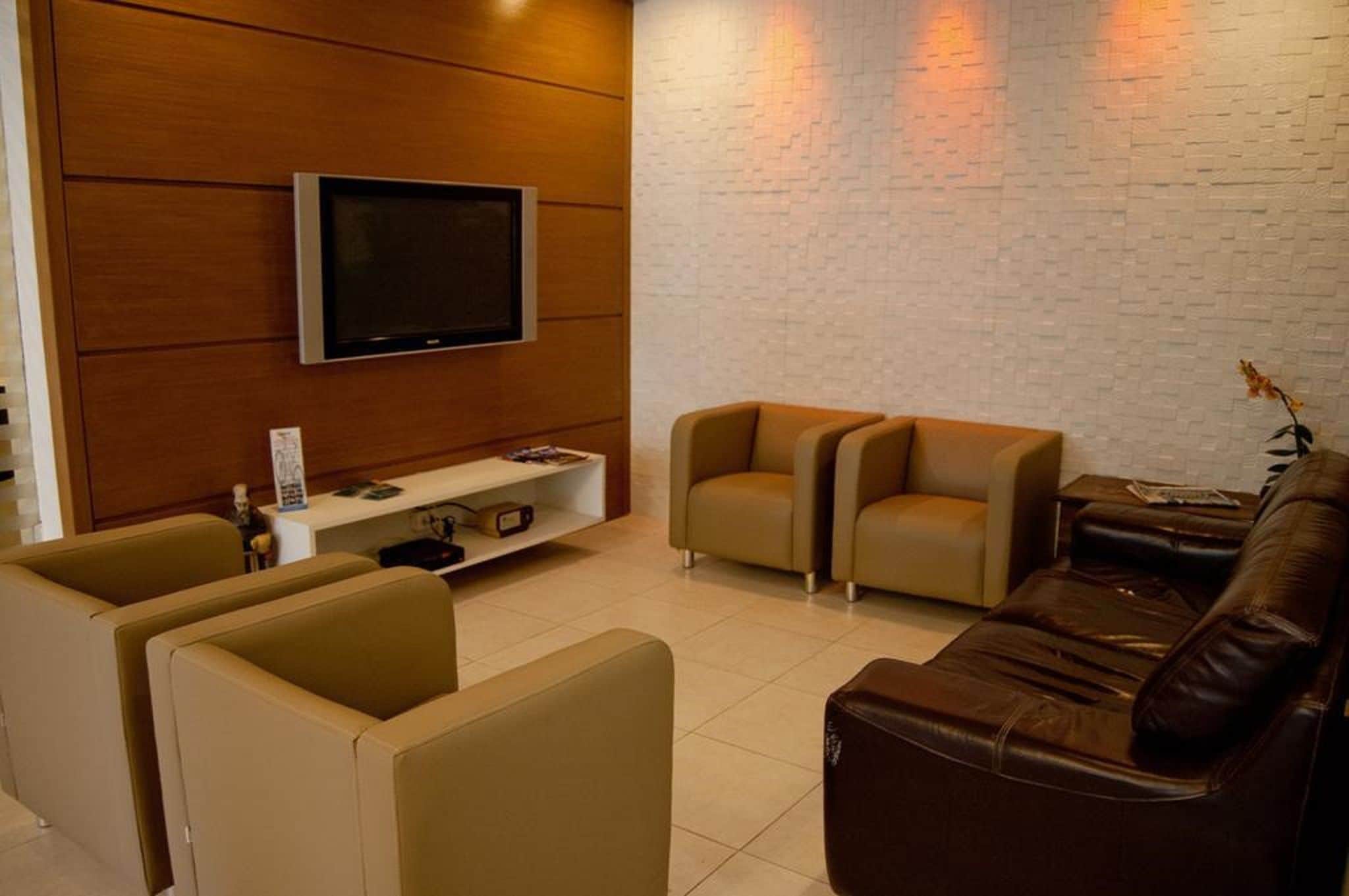 Una sala de estar moderna con una televisión de pantalla plana, un panel de pared de madera, una pared de ladrillo blanco y un sofá de cuero marrón.