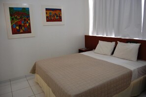 A hotel room with a bed, a nightstand, and two framed paintings on the wall. - Rede Andrade Navegantes (Recife)