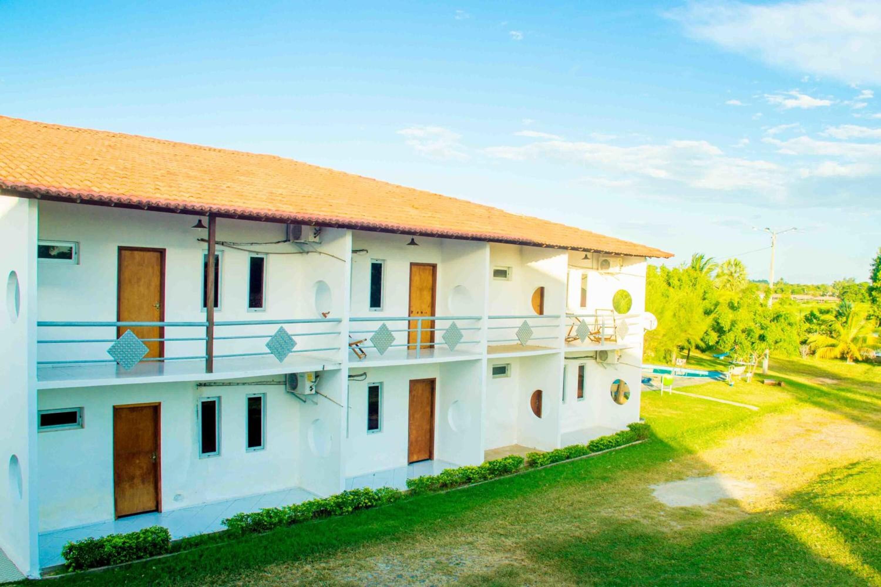 A white building with a tiled roof, multiple balconies, and a grassy courtyard.