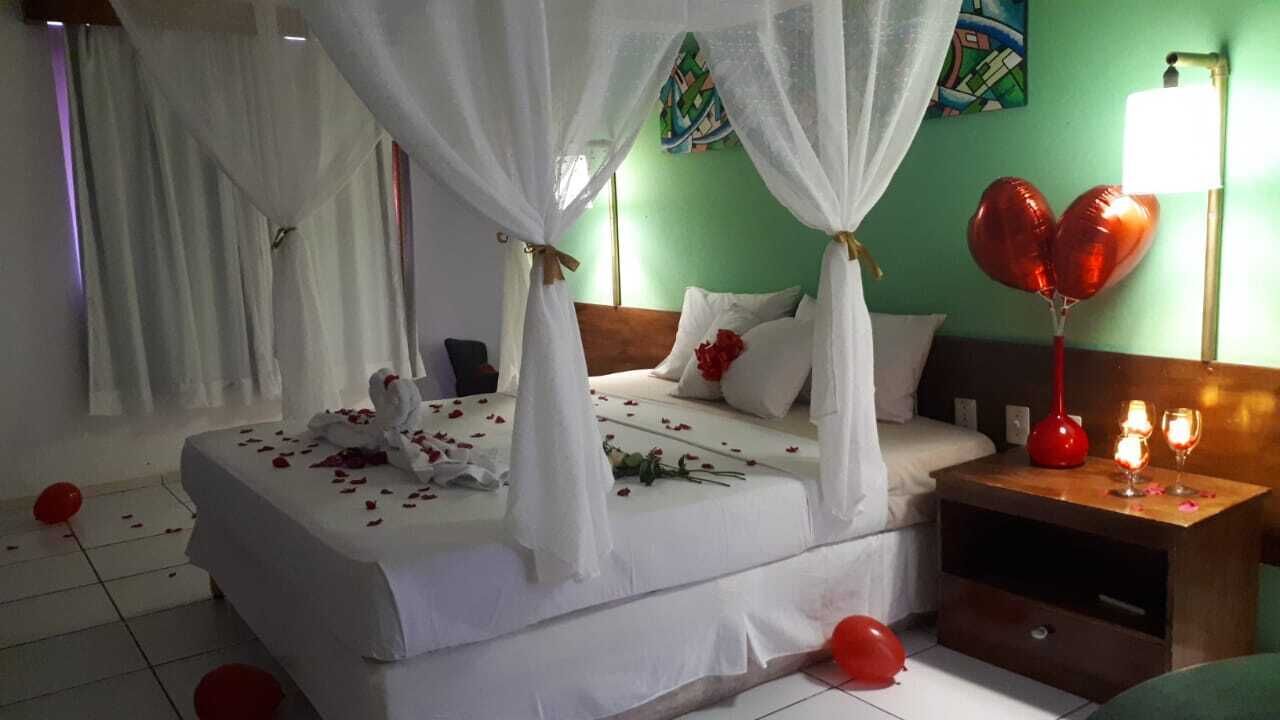 Una cama con dosel, una mesita de noche con lámpara y globos rojos en el suelo.