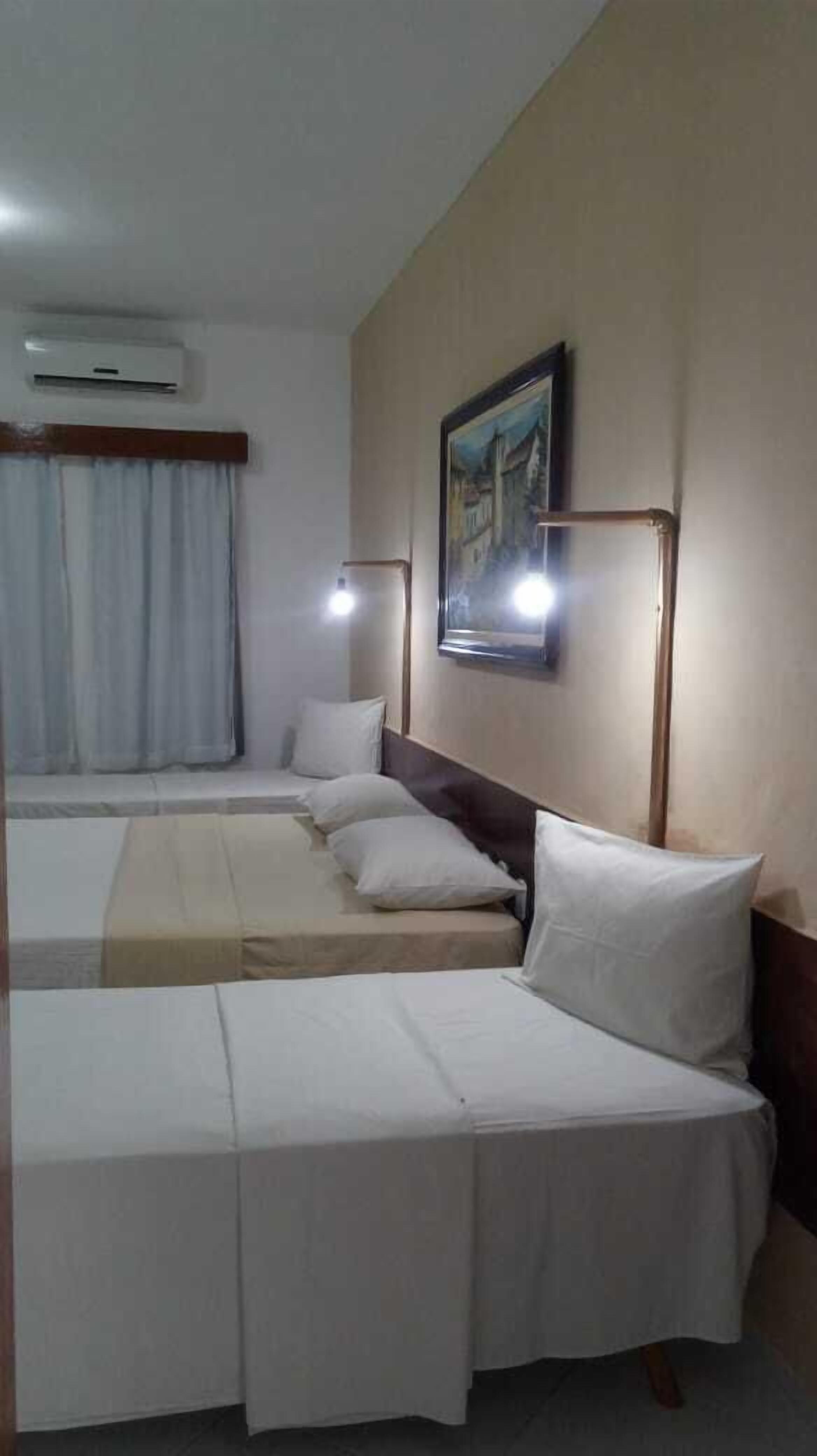 Habitación de hotel con dos camas individuales, un cuadro en la pared y un equipo de aire acondicionado sobre la ventana.