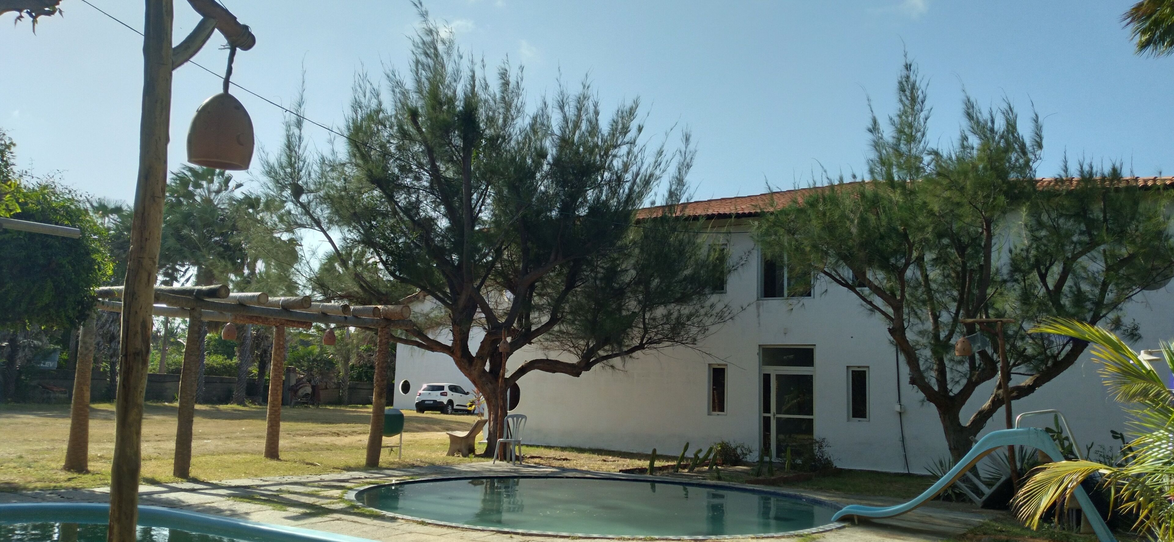 A swimming pool with a slide, a white building with a red roof, and a car parked nearby.