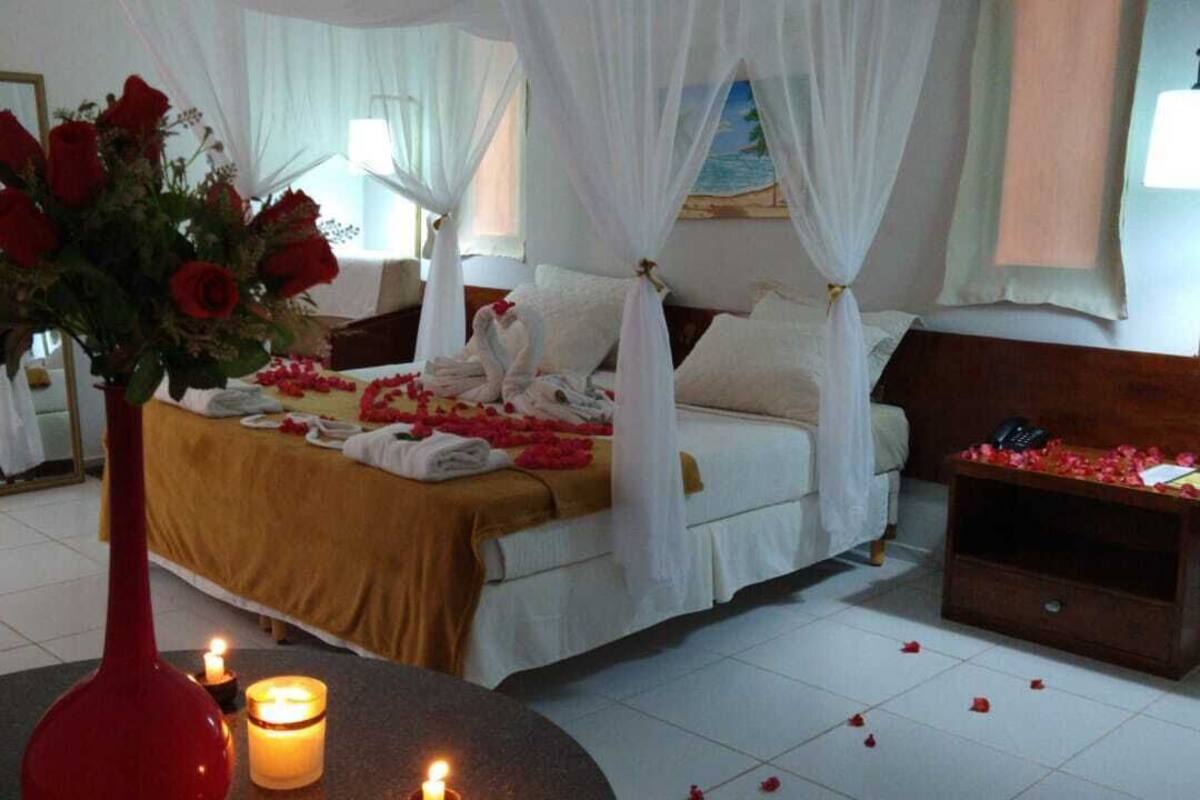 A bedroom with a four-poster bed, a bedside table with a vase of red roses, and a mirror on the wall.