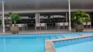 A pool area with a tiled deck, white tables, and chairs, surrounded by potted plants. - Hotel Executive Flat Arrey (Teresina)