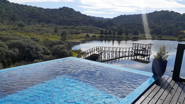 Una piscina con cubierta de madera y vista a un lago rodeado de colinas.