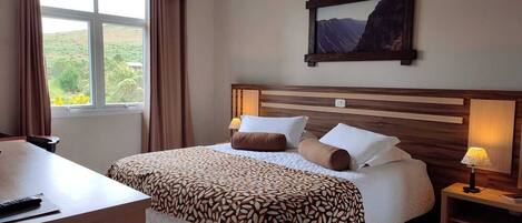 A hotel room with a large bed, a desk, a chair, a nightstand with a lamp, and a painting on the wall.