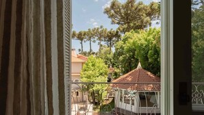 A balcony with a view of a swimming pool, a pergola, and surrounding trees. - Pousada Doce Canela (Canela)
