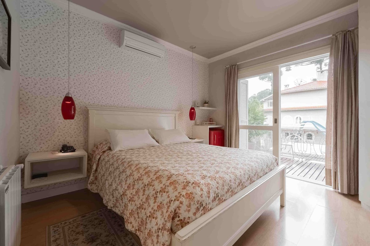 A bedroom with a bed, nightstands, a red lamp, a radiator, and a view of the outside.