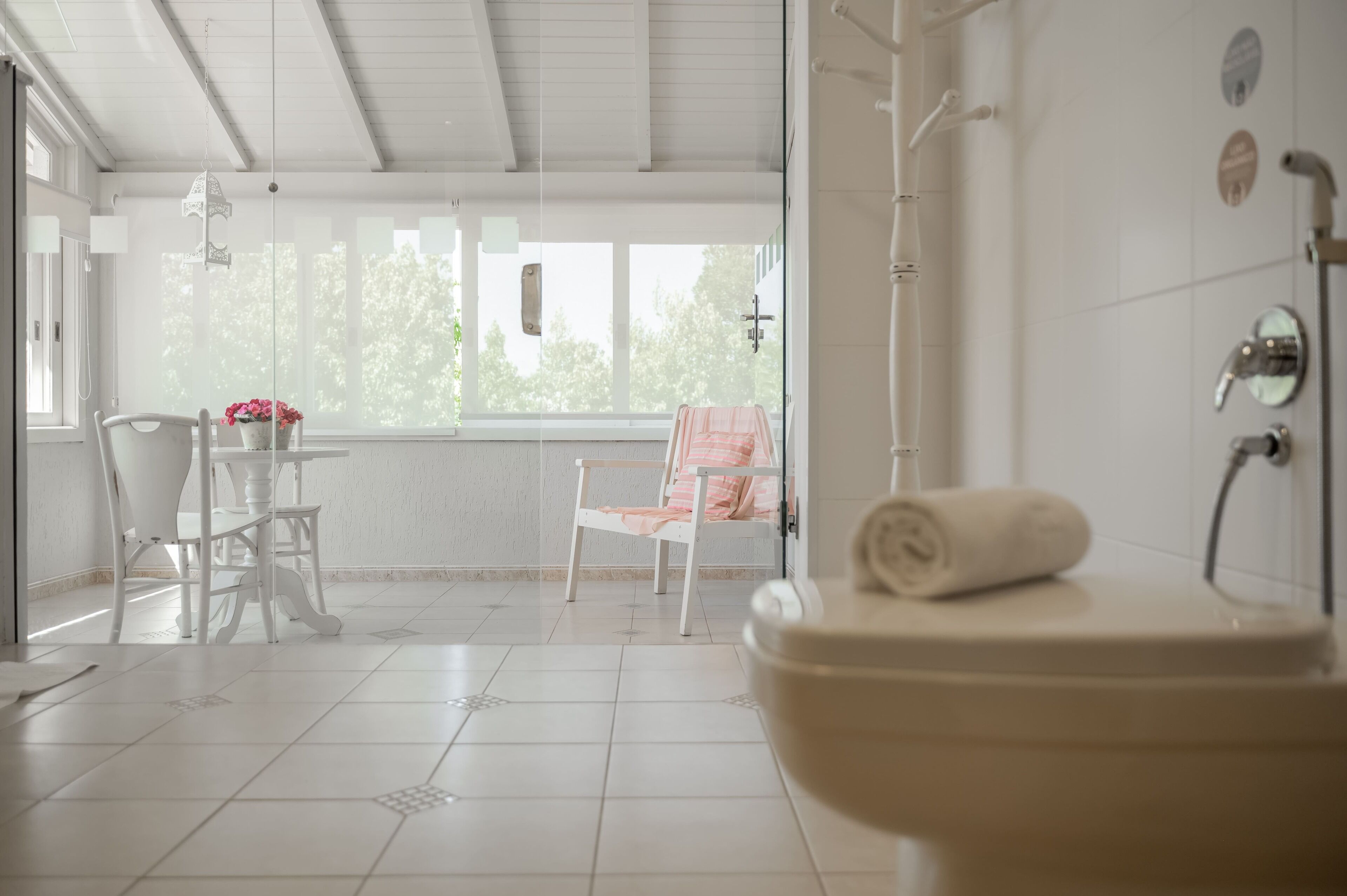 Een badkamer met toilet, douche en een stoel bij een raam.