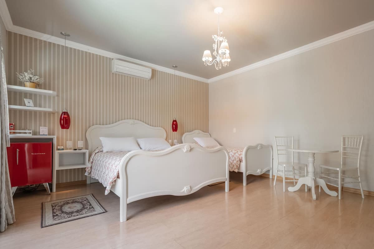 A bedroom with a bed, a red wardrobe, a white table with chairs, and a chandelier.