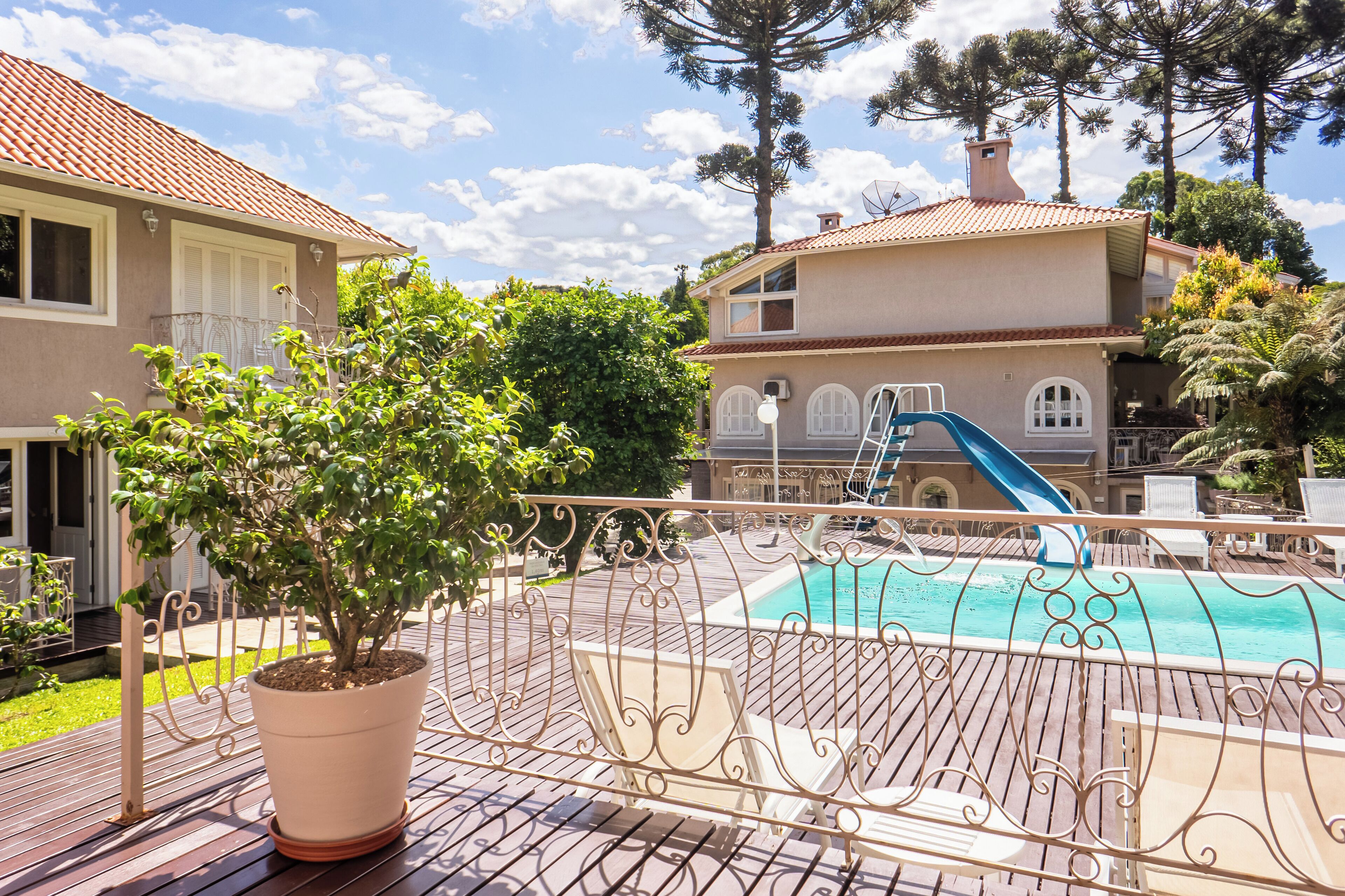 Zona de piscina con tobogán, planta en maceta y barandilla.