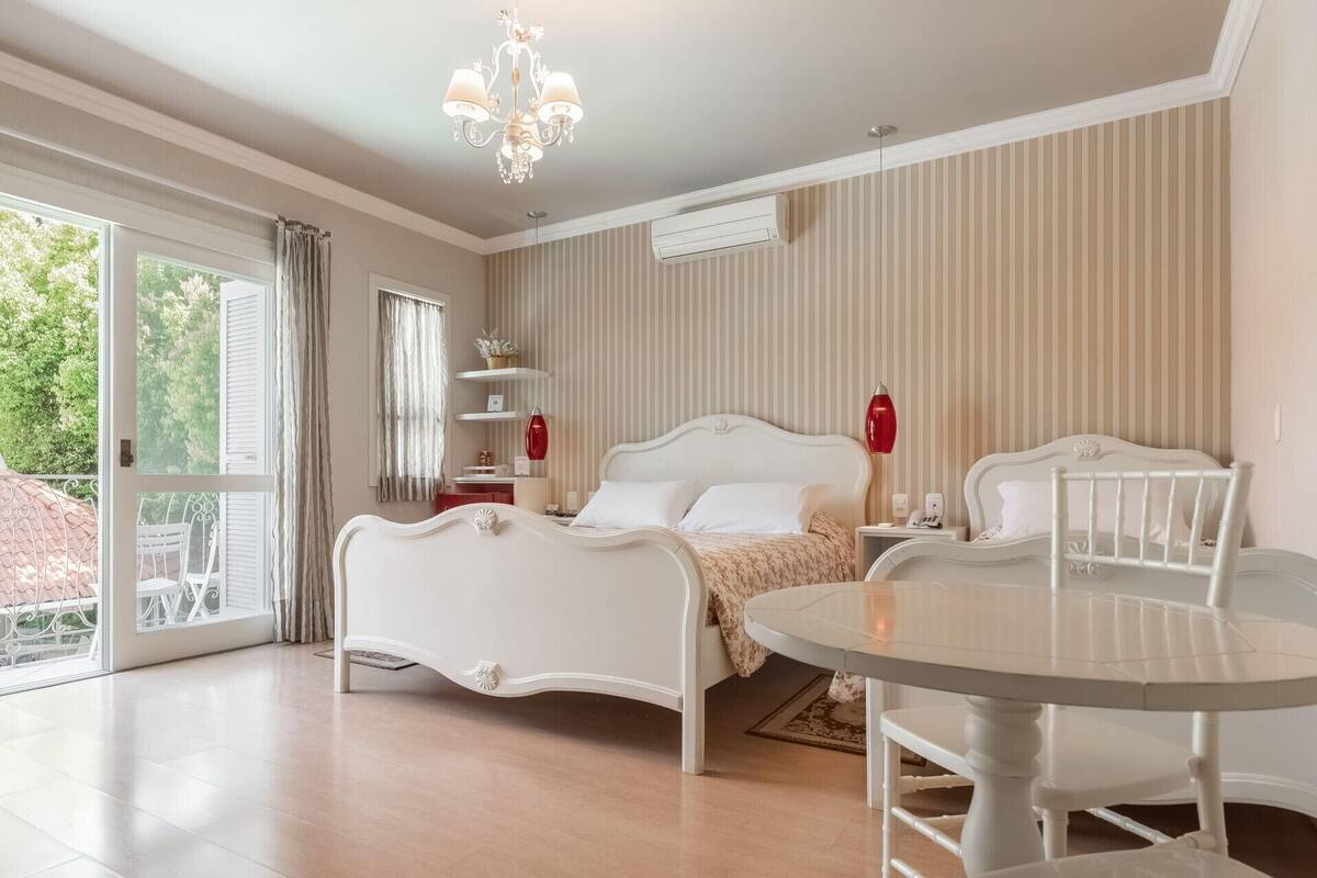 A bedroom with a bed, bedside table, lamp, and a view of the outdoors.