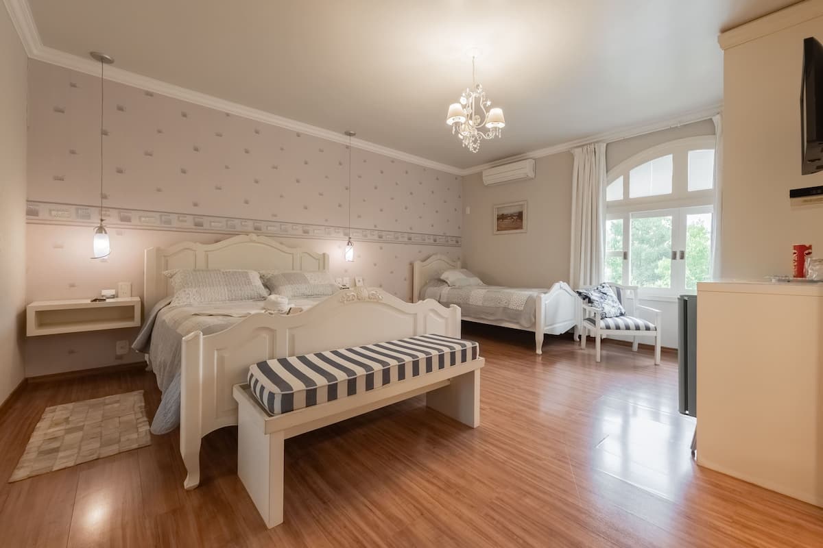 A bedroom with a bed, bedside tables, a bench, a chair, a TV, and a window.