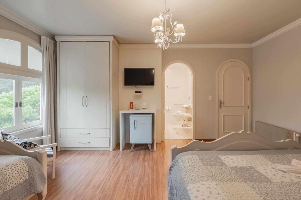 A bedroom with a bed, a wardrobe, a television, and a bathroom visible through an archway.