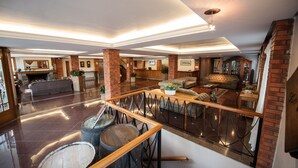 Een ruime lobby met een hoge plafond, een receptiebalie, een open haard en een zithoek met banken en een salontafel.