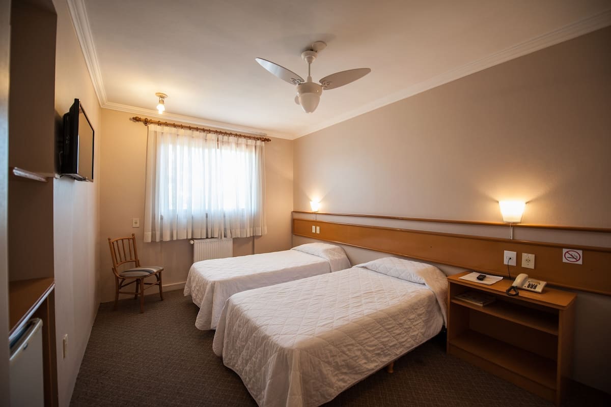 Habitación de hotel con dos camas, ventilador de techo, escritorio con teléfono y una silla.