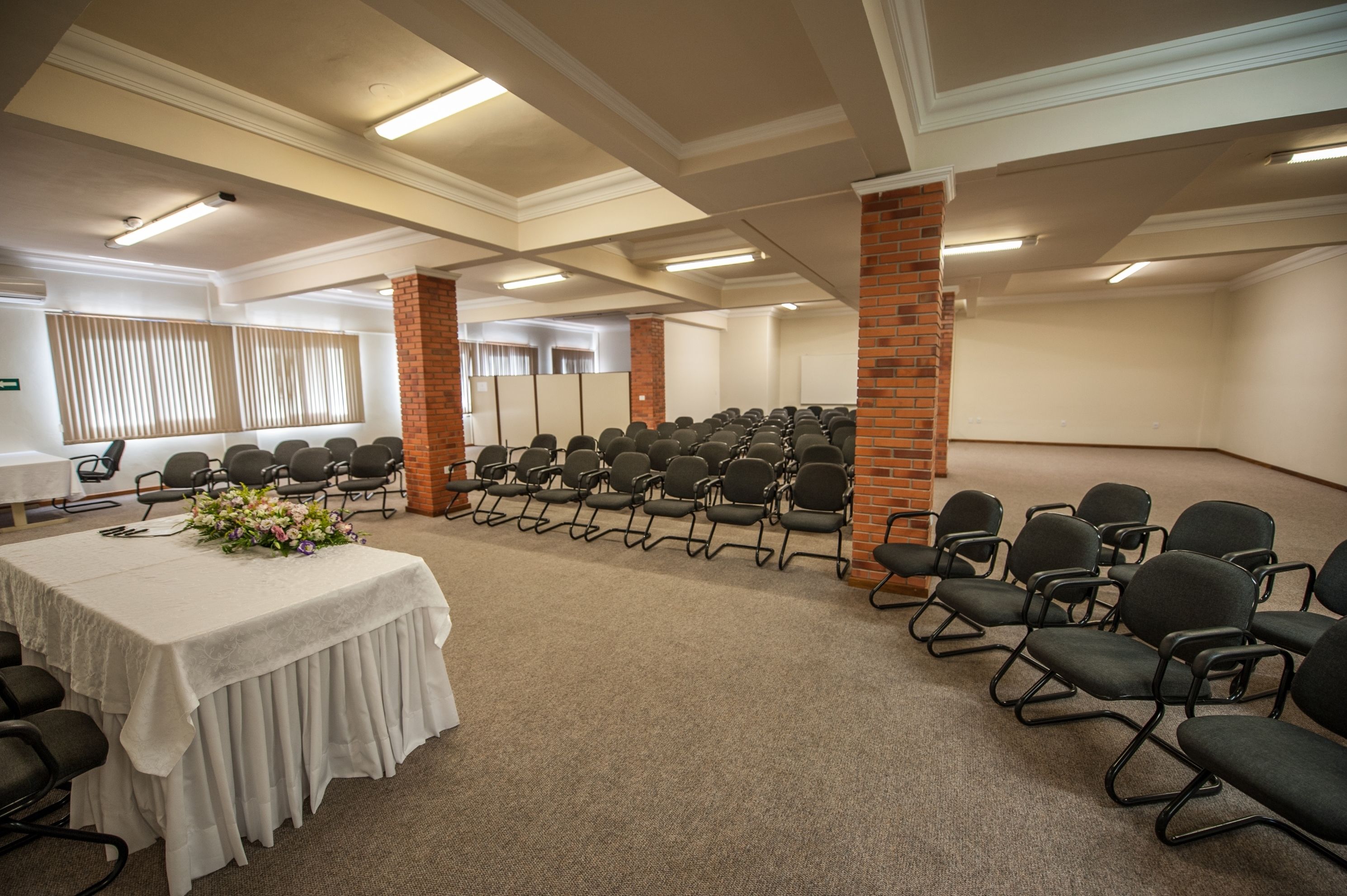 Un salón de conferencias con una larga mesa, filas de sillas y piso alfombrado.