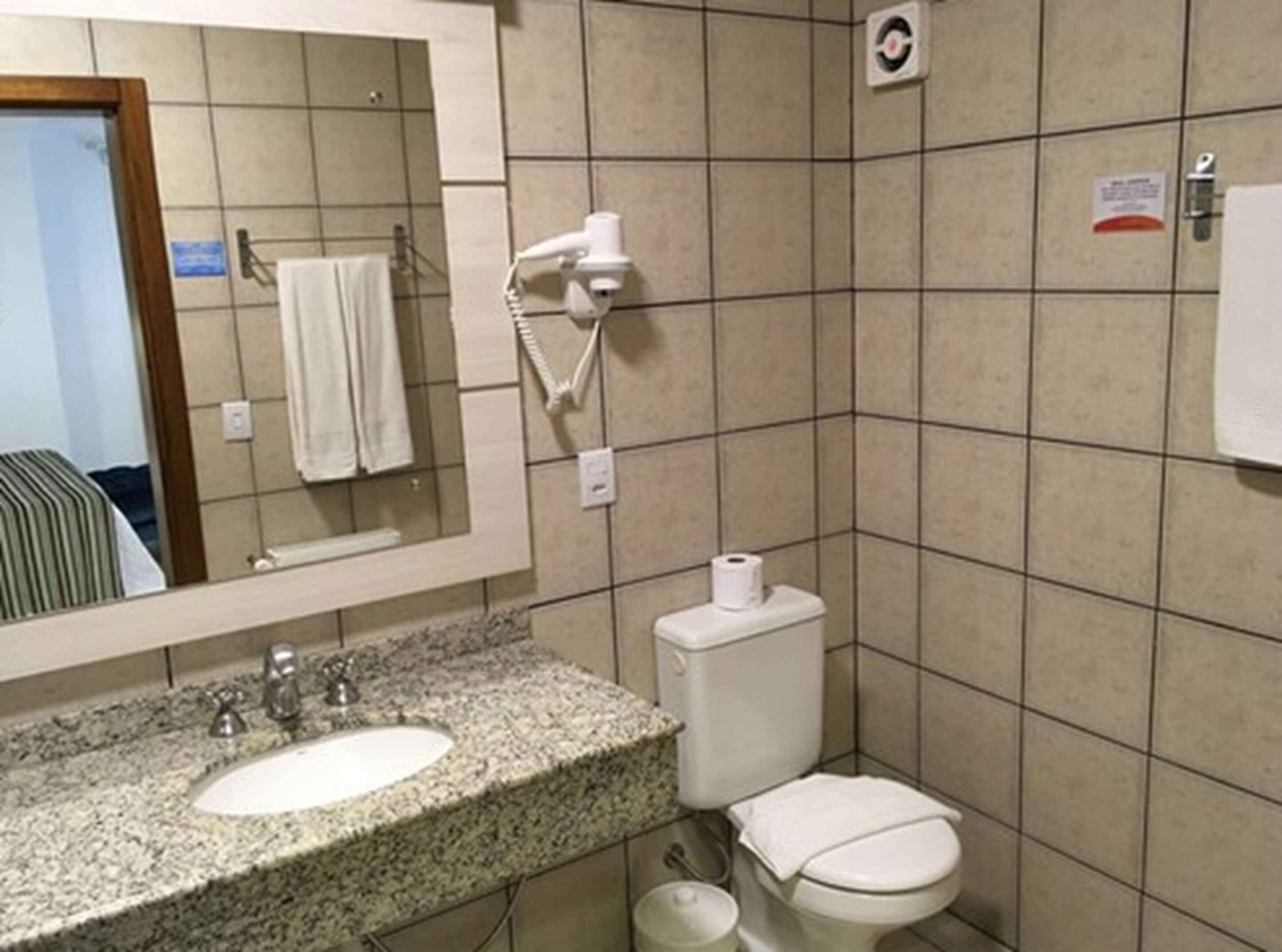 Casa de banho com lavatório com bancada de granito, sanita branca e secador de cabelo fixado na parede.