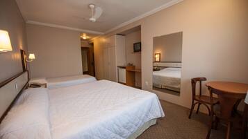 Quarto de hotel com duas camas, uma escrivaninha, uma cadeira, um ventilador de teto e uma televisão.