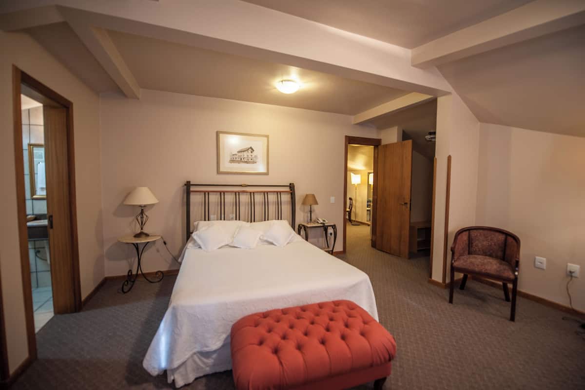 Un dormitorio con una cama grande, una mesita de noche, una silla y una puerta que da a otra habitación.