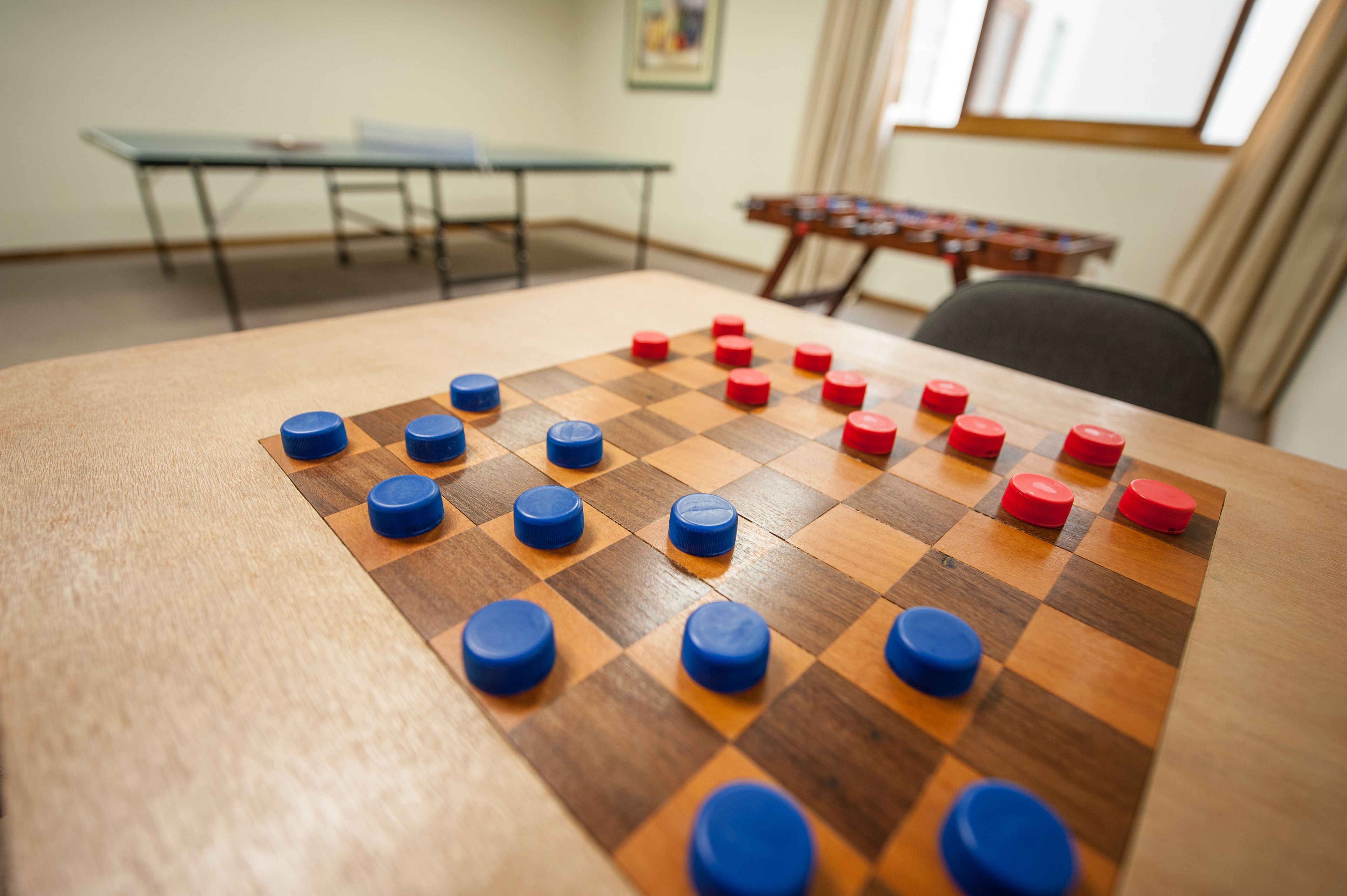 Un juego de mesa con tablero de cuadros, piezas rojas y azules, una mesa y una ventana al fondo.