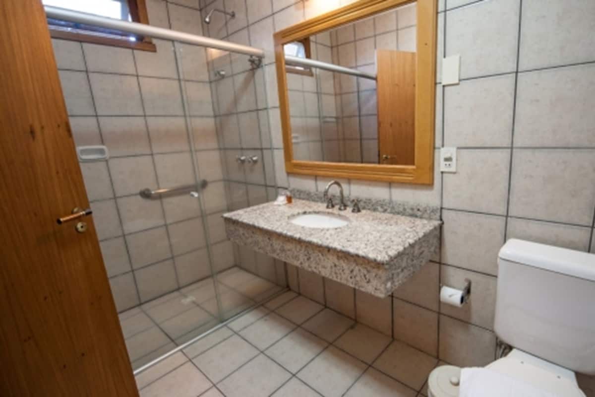 Un baño con cabina de ducha de vidrio, lavamanos con encimera de granito, espejo con marco de madera y inodoro blanco.