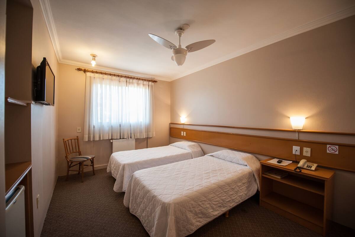 Habitación de hotel con dos camas individuales, ventilador de techo, escritorio con teléfono y una silla.