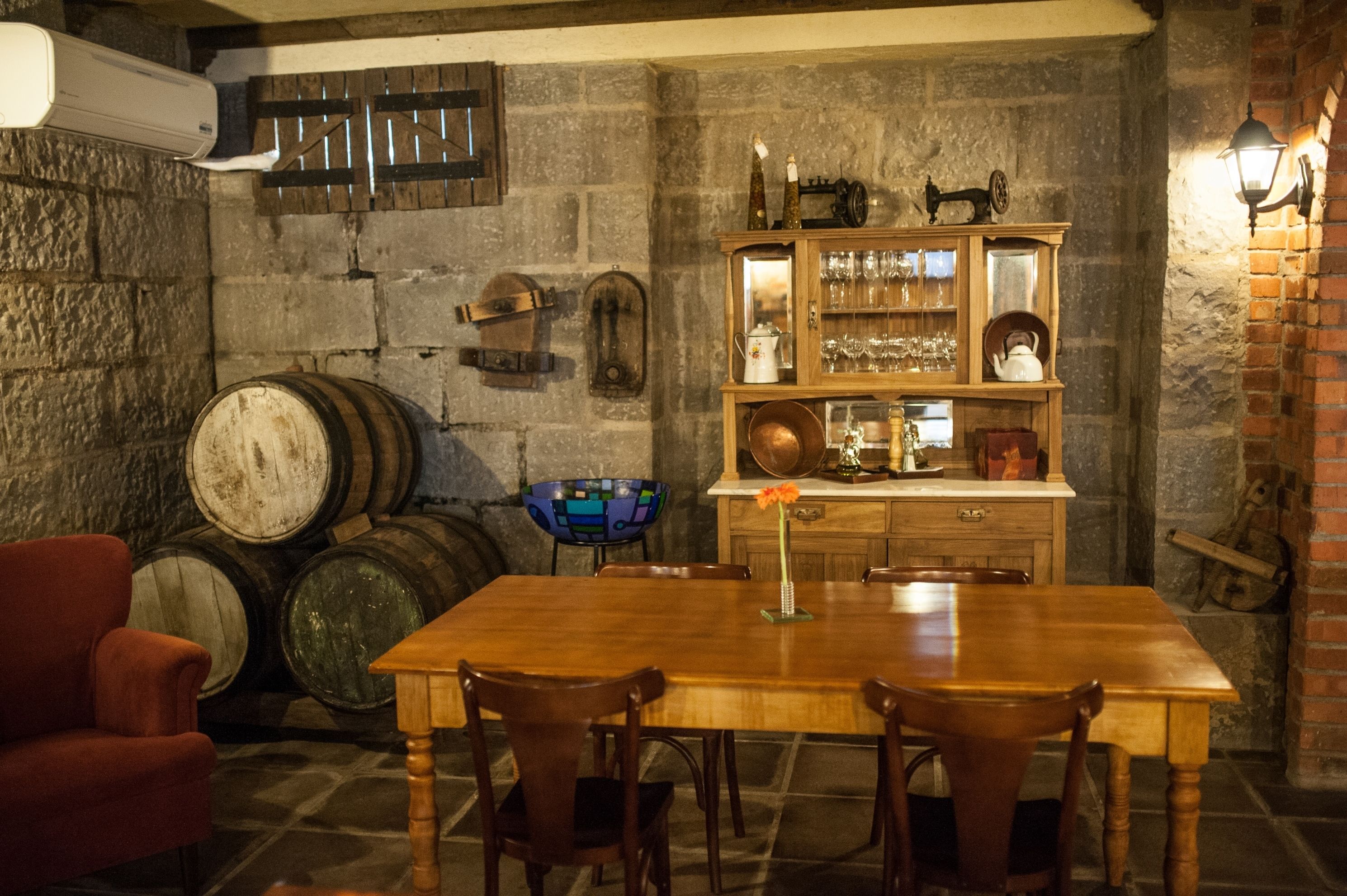 A rustic dining area with a wooden table and chairs, surrounded by stone walls and wooden barrels.