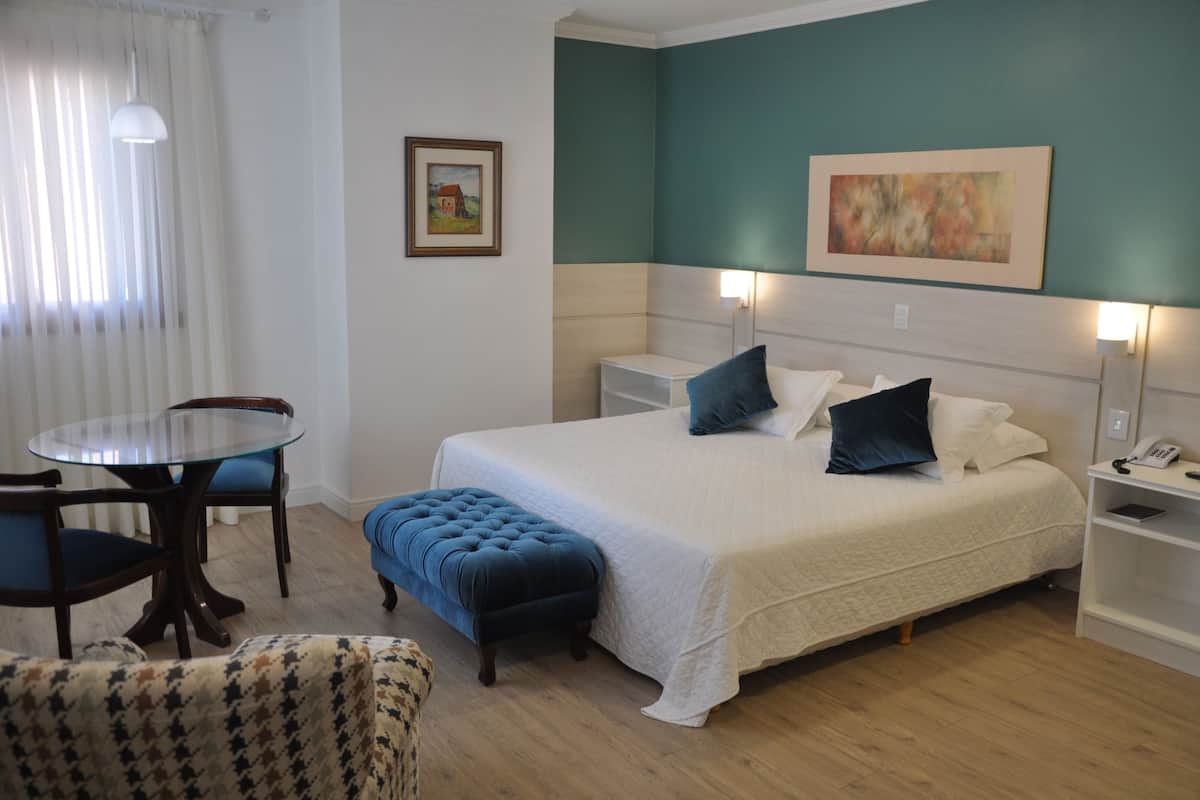 Un dormitorio ordenado con cama, mesitas de noche, una pequeña mesa y sillas.