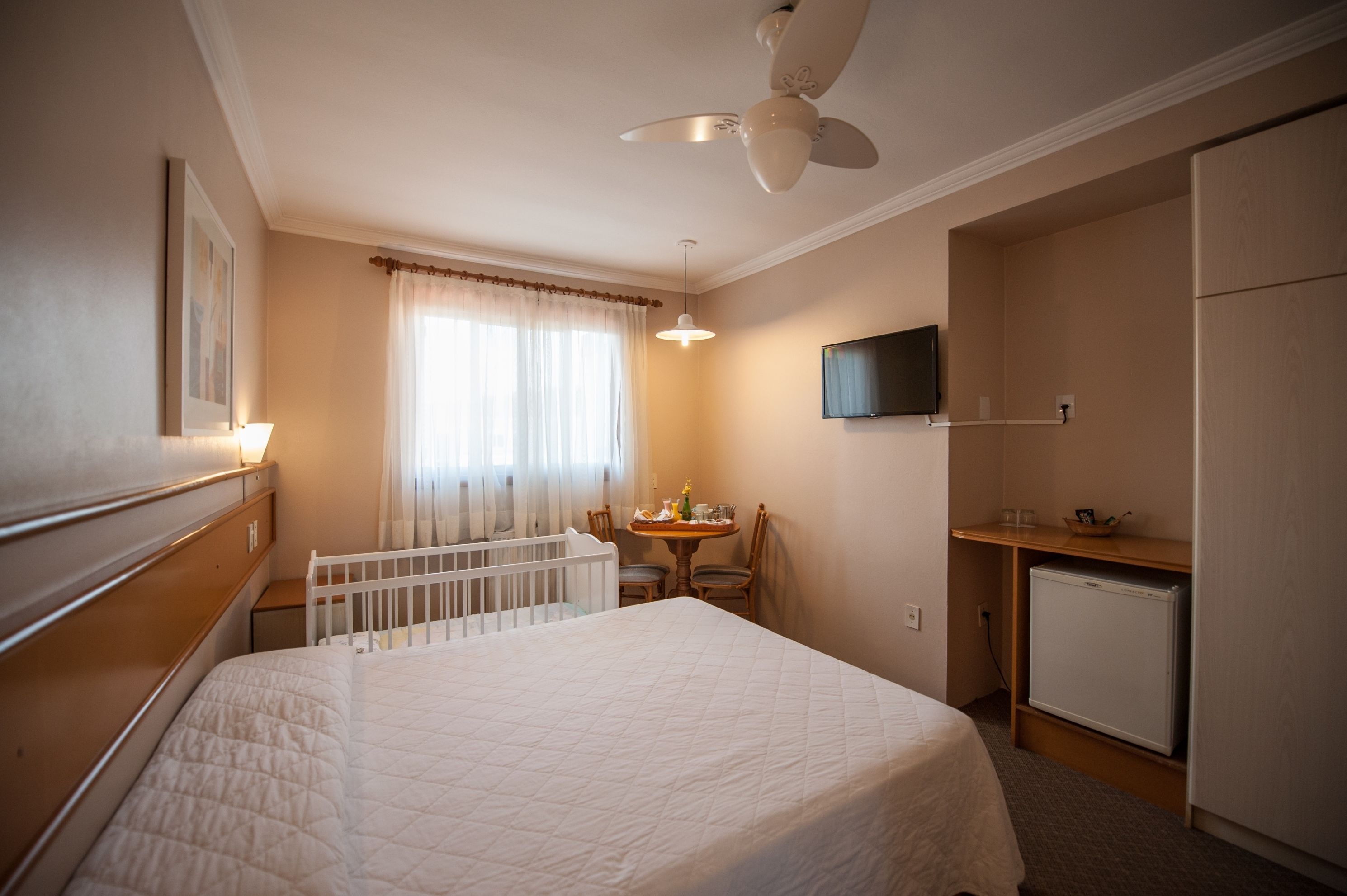 Habitación de hotel con cama, cuna, mesa de comedor con sillas, televisión y refrigerador.