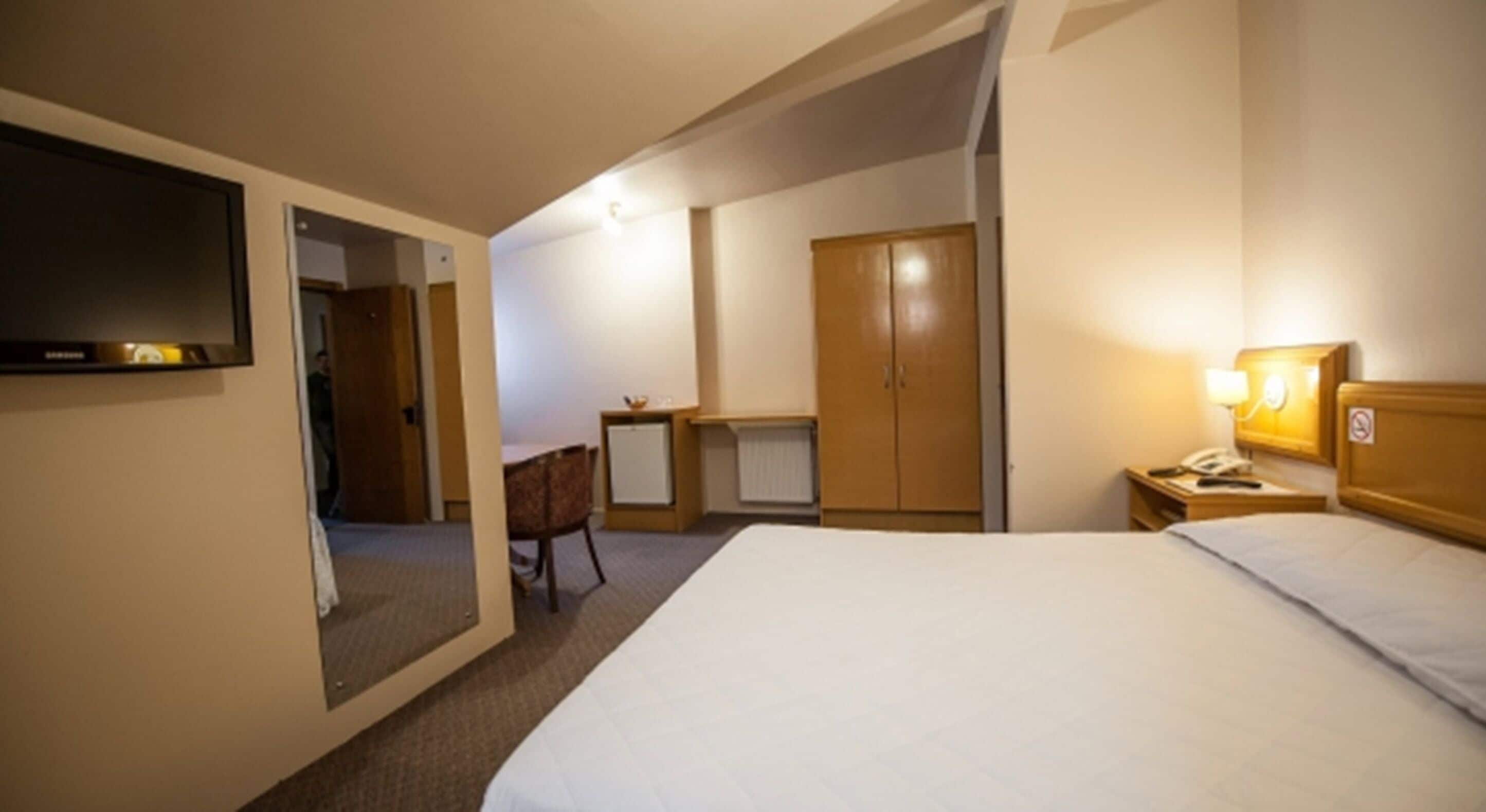 A hotel room with a bed, a desk, a chair, a wardrobe, and a television.