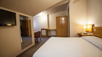 A hotel room with a bed, a desk, a chair, a wardrobe, and a television.
