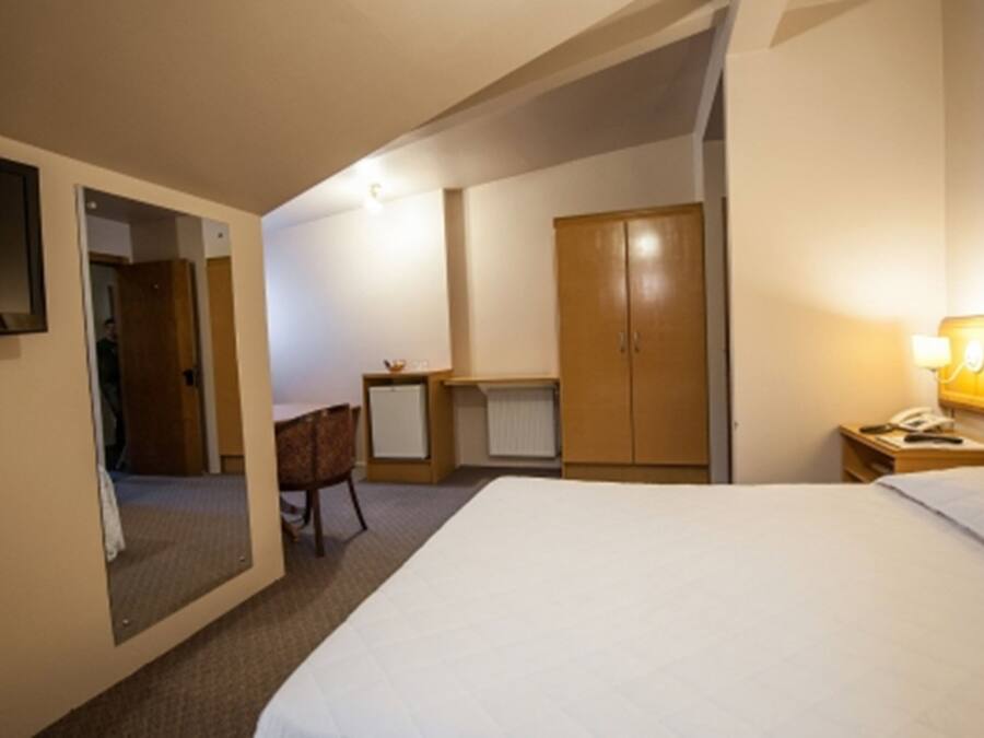 A hotel room with a bed, a desk, a chair, a wardrobe, and a television.