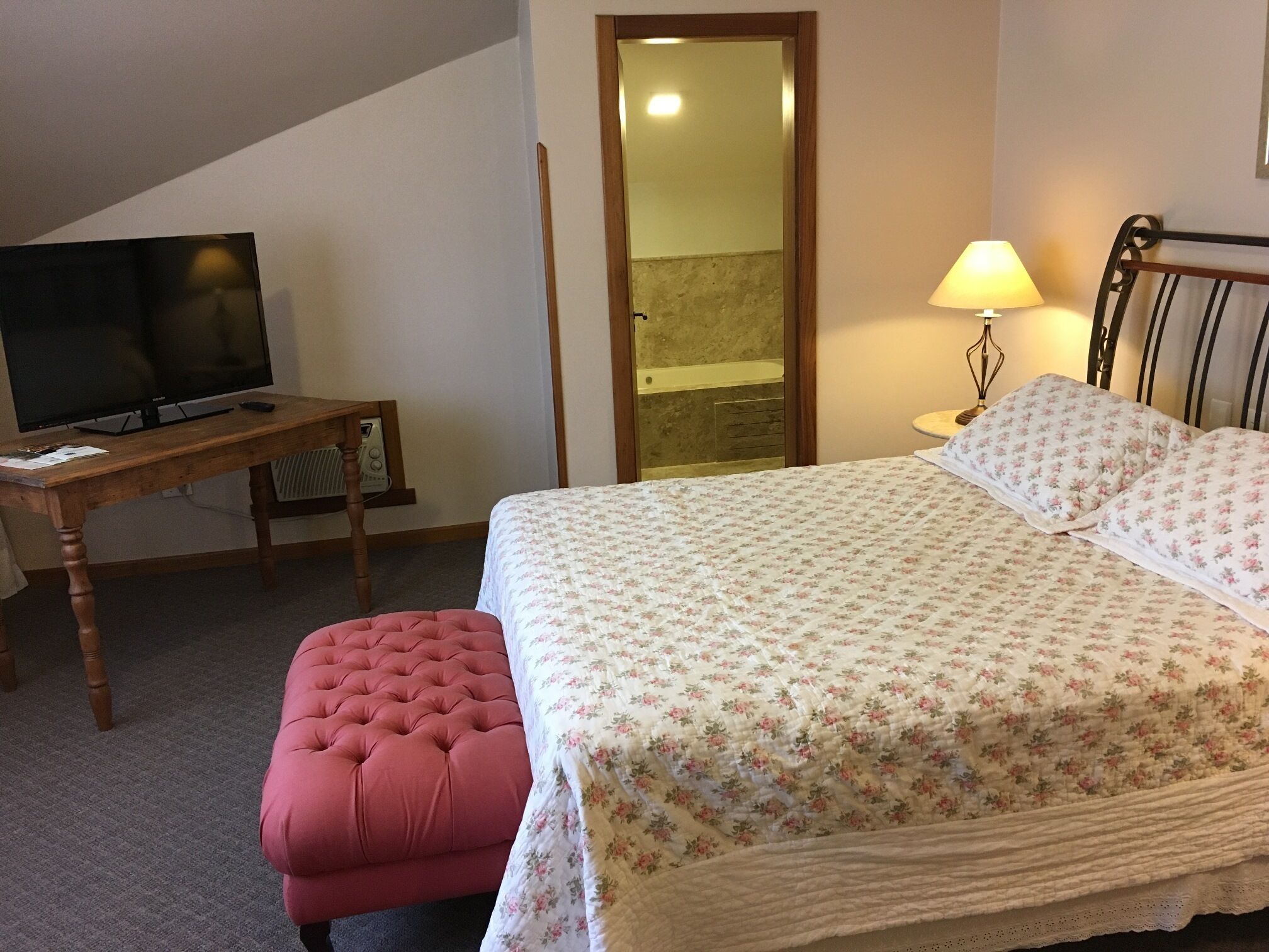 Een slaapkamer met een bed, een televisie op een houten tafel, een lamp en een klein krukje.