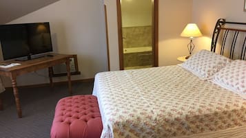 Een slaapkamer met een bed, een televisie op een houten tafel, een lamp en een klein krukje.