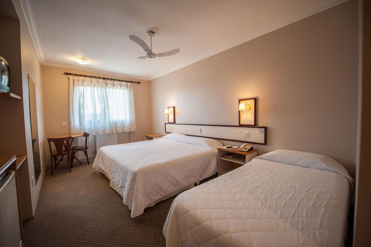 Habitación de hotel con dos camas, un escritorio, una silla, un ventilador de techo y una ventana con cortinas.
