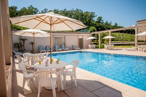 Un espace piscine avec des chaises longues blanches, des parasols et une table où sont servis des boissons.