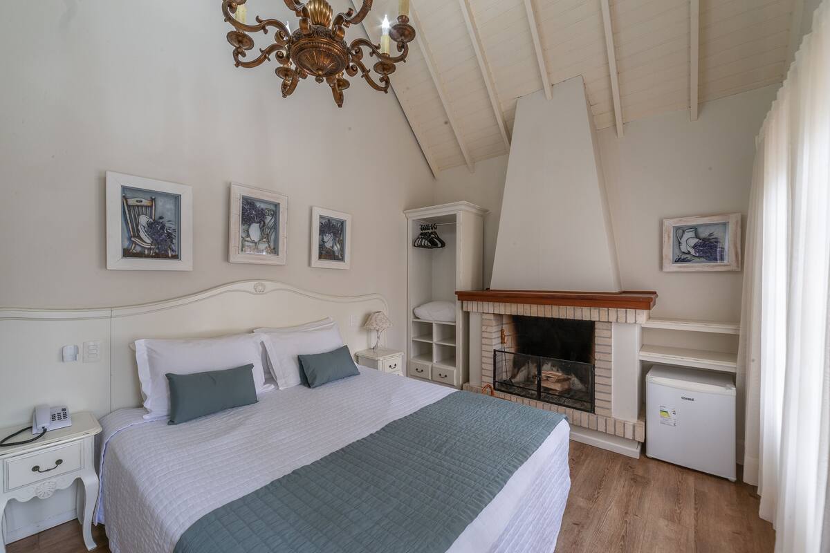 A bedroom with a large bed, a fireplace, and framed artwork on the walls.