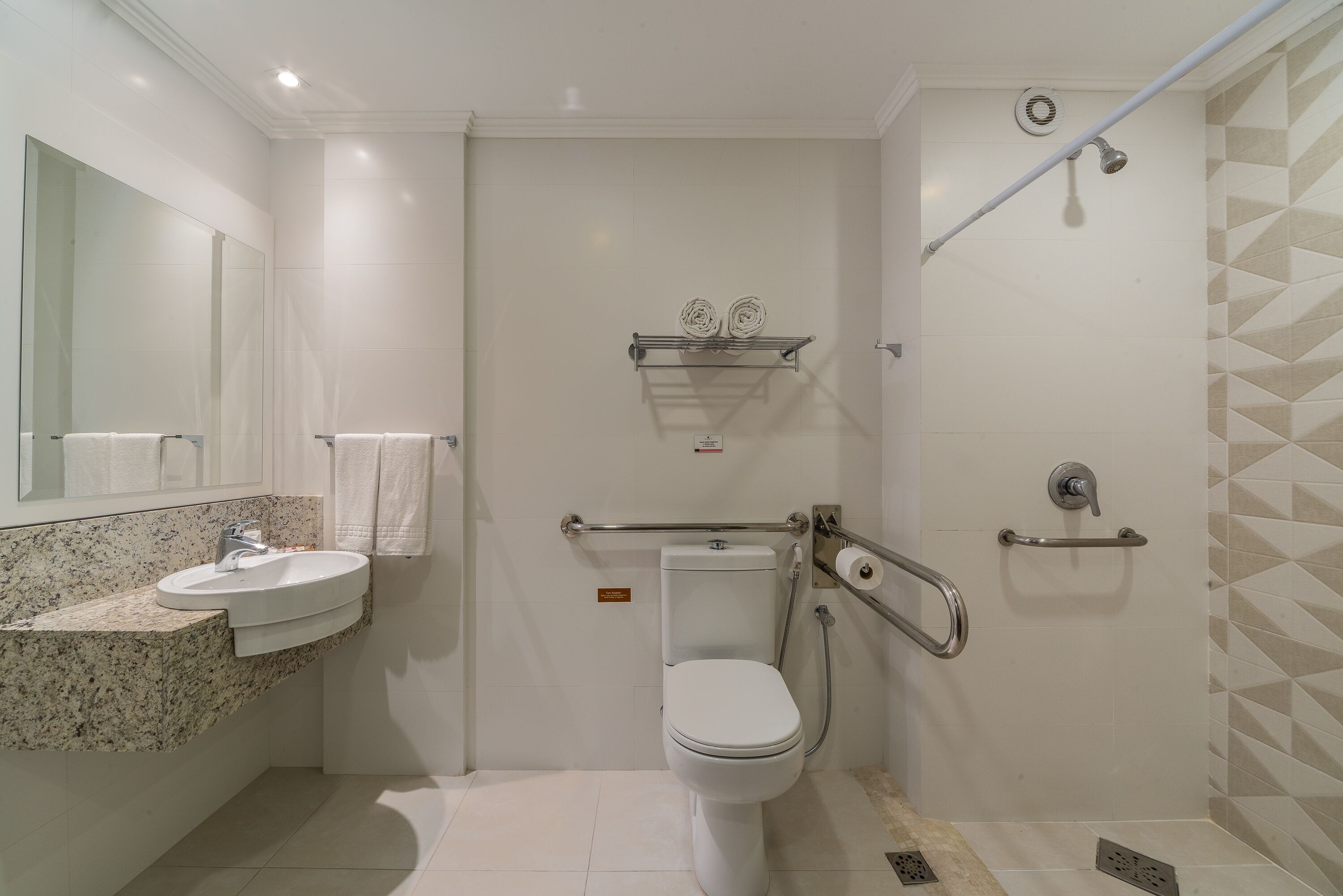 Un baño moderno con inodoro blanco, lavamanos de encimera de granito, espejo y zona de ducha.