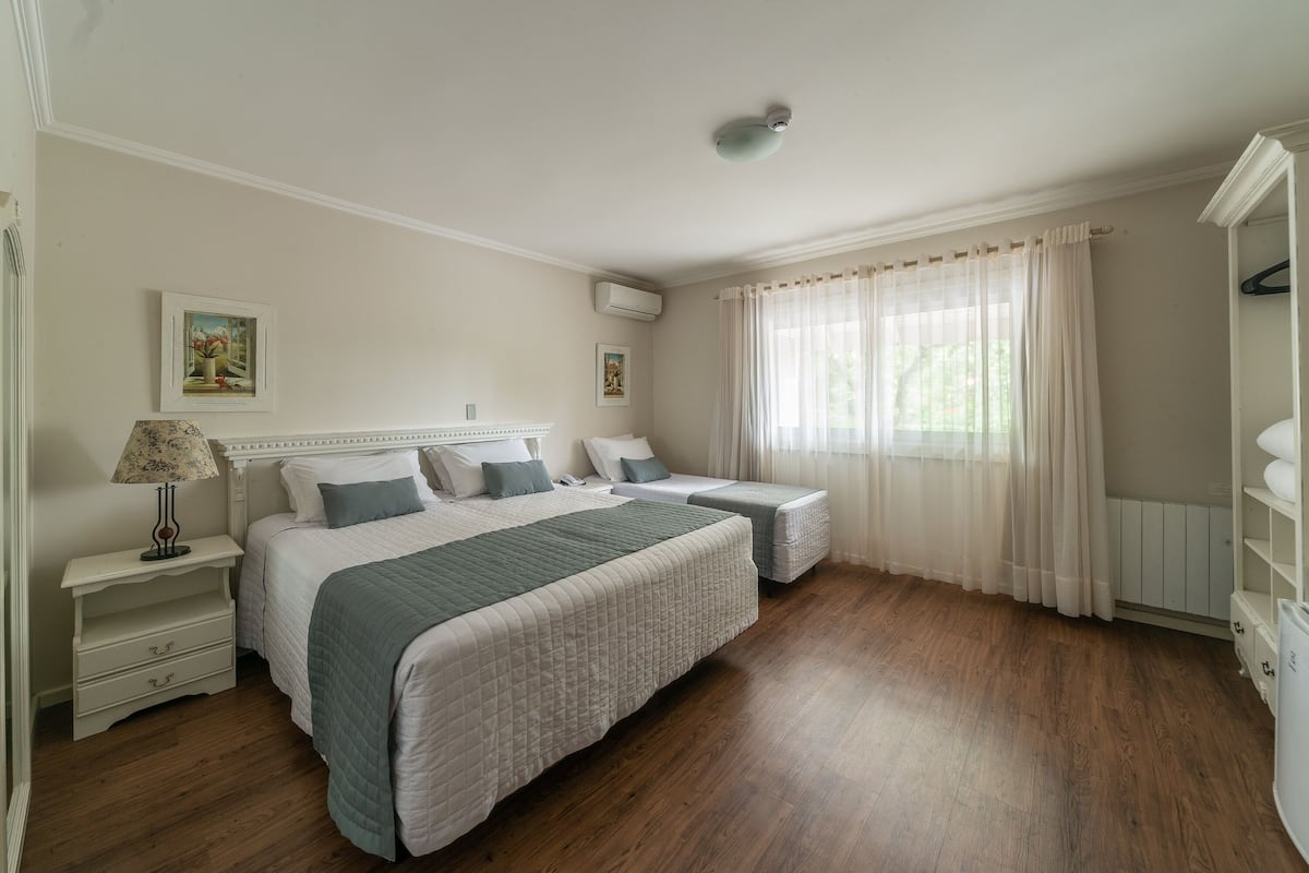 A bedroom with two beds, a nightstand with a lamp, and a window with sheer curtains.
