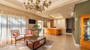 Un vestíbulo de hotel con una mesa de recepción, dos sillones, una mesita de café, una araña y una planta grande.