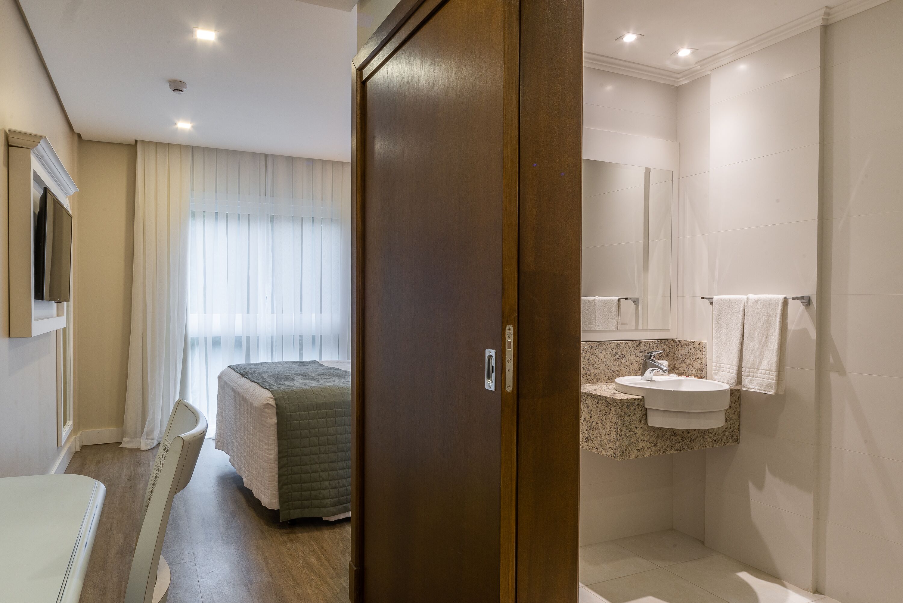 Een hotelkamer met een bed, een badkamer met een wastafel en spiegel, en een deur met een handvat.