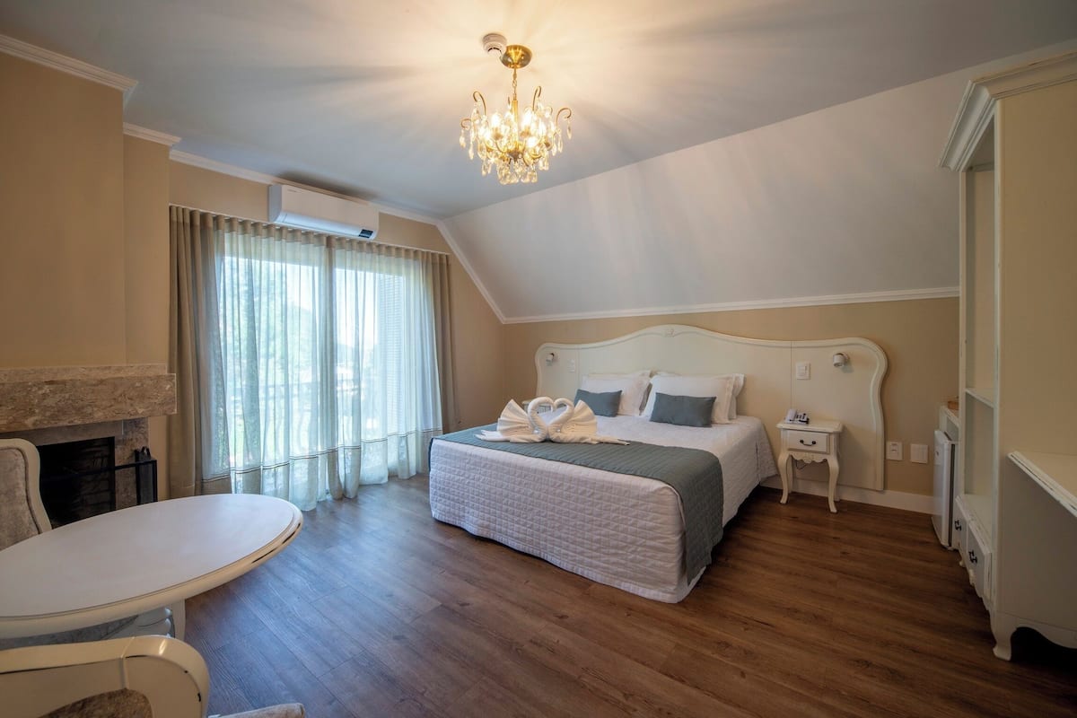 A bedroom with a large bed, a bedside table, a chair, a chandelier, and a fireplace.