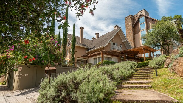 Un hotel moderno con una escalera de piedra que conduce a un vestíbulo cubierto, rodeado de abundante vegetación y un cielo despejado.