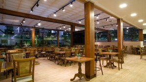 Un amplio comedor interior con mesas y sillas de madera, ventanas grandes y un techo alto con iluminación empotrada.