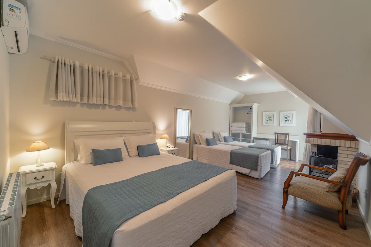 A bedroom with two beds, a piano, a chair, and a fireplace.