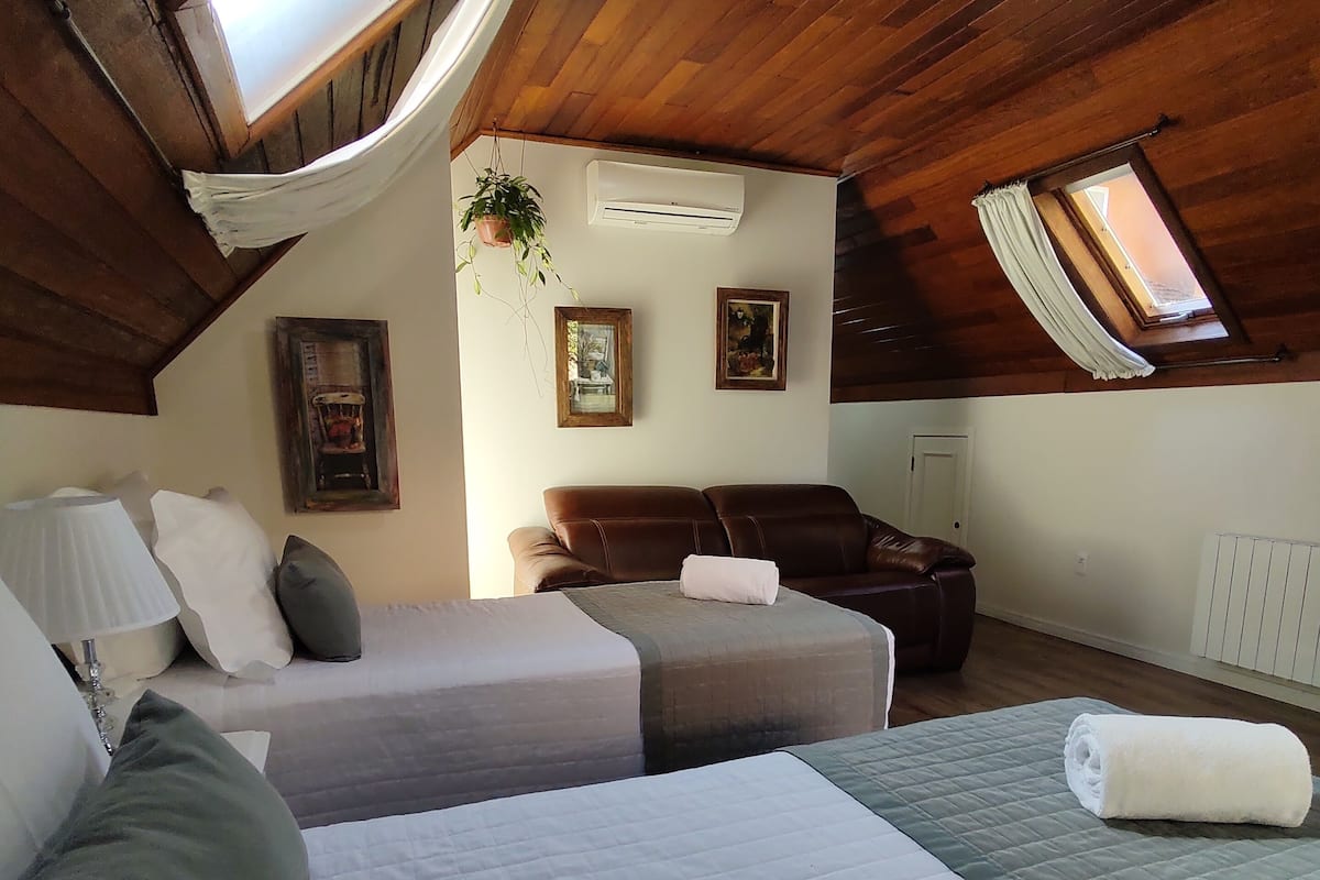 A cozy attic bedroom with two beds, a sofa, and a hanging plant.