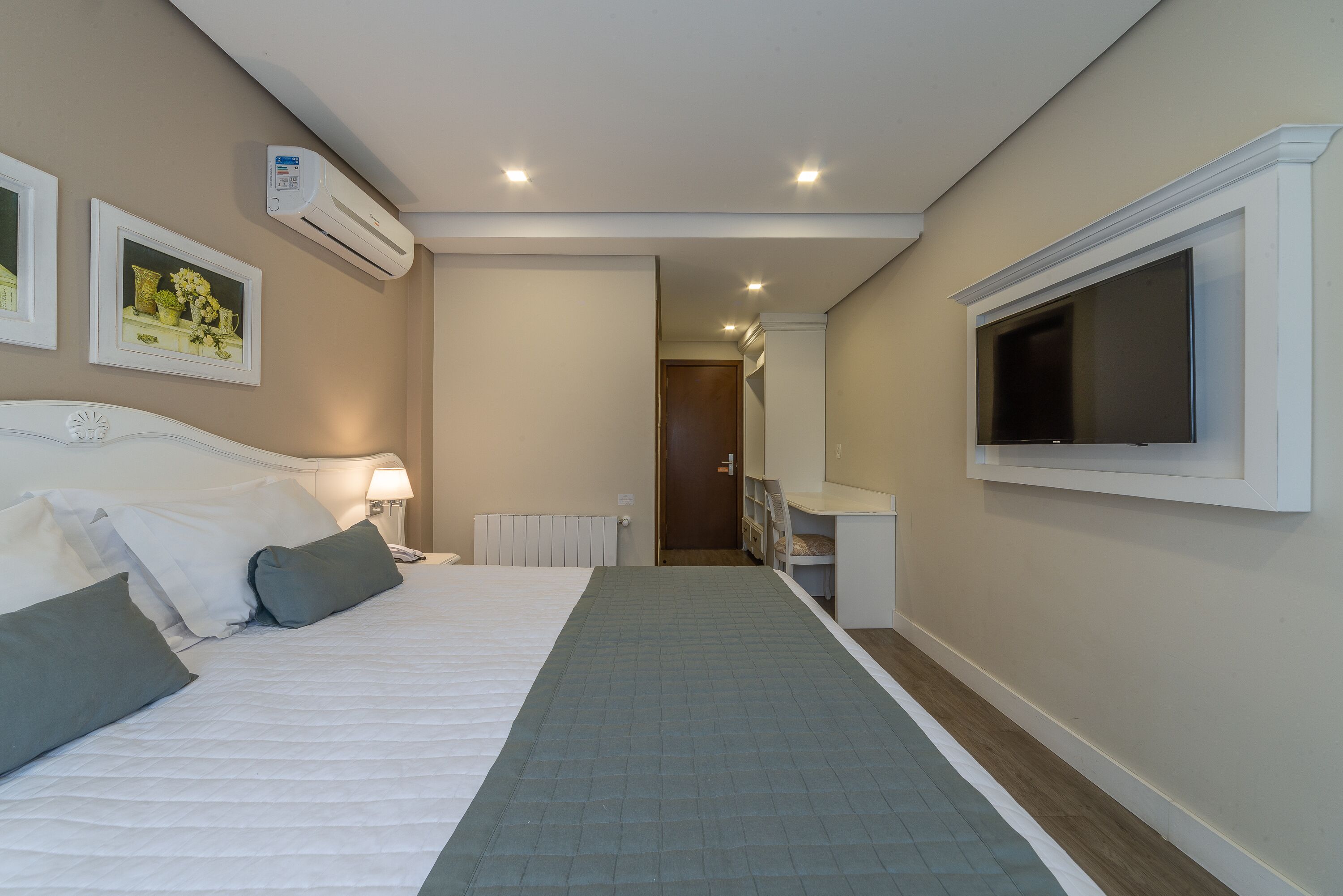 Una habitación de hotel con cama, televisor, aire acondicionado y cuadros en la pared.