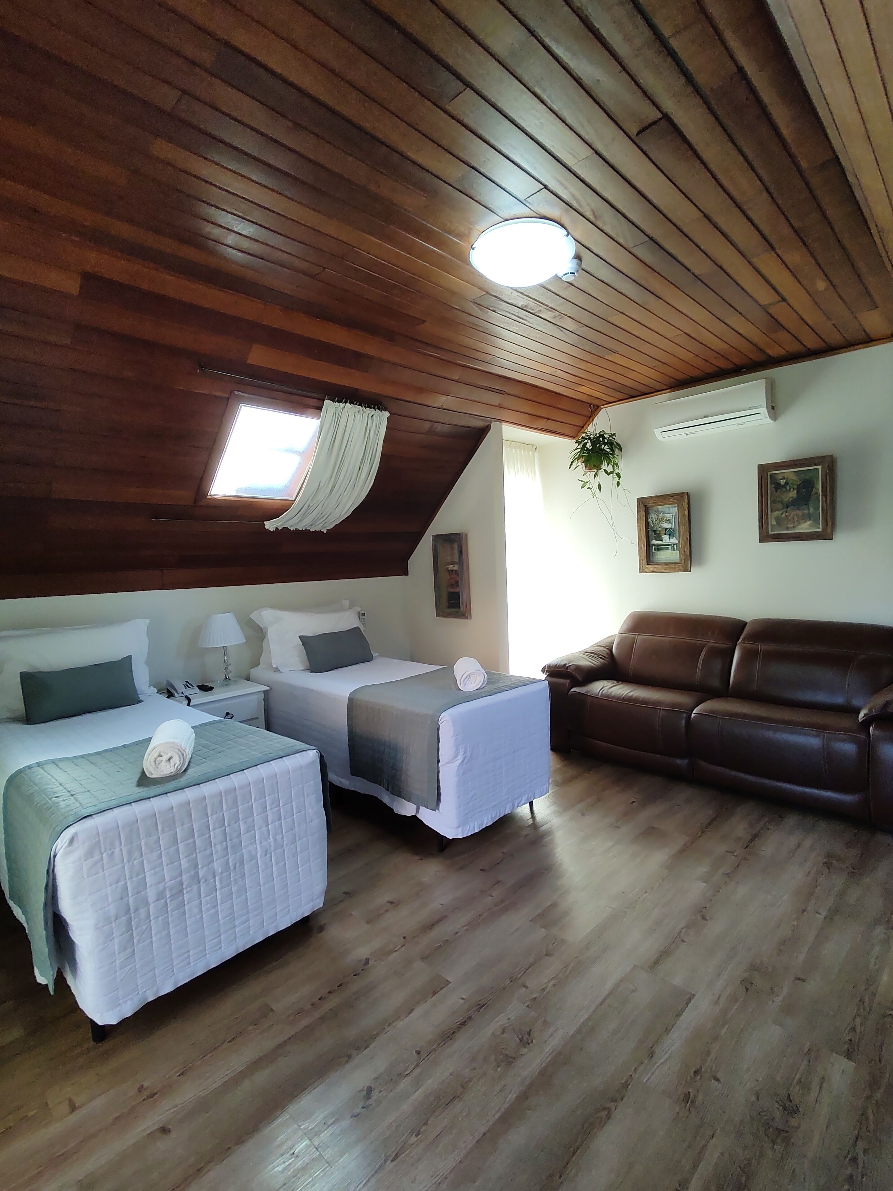 A cozy room with two beds, a brown leather sofa, wooden flooring, a ceiling fan, and a window with curtains.
